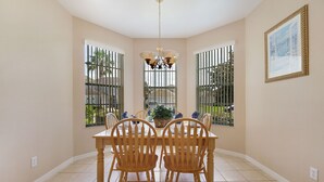 A dining area with a wooden table and chairs, a chandelier, and a view through barred windows.