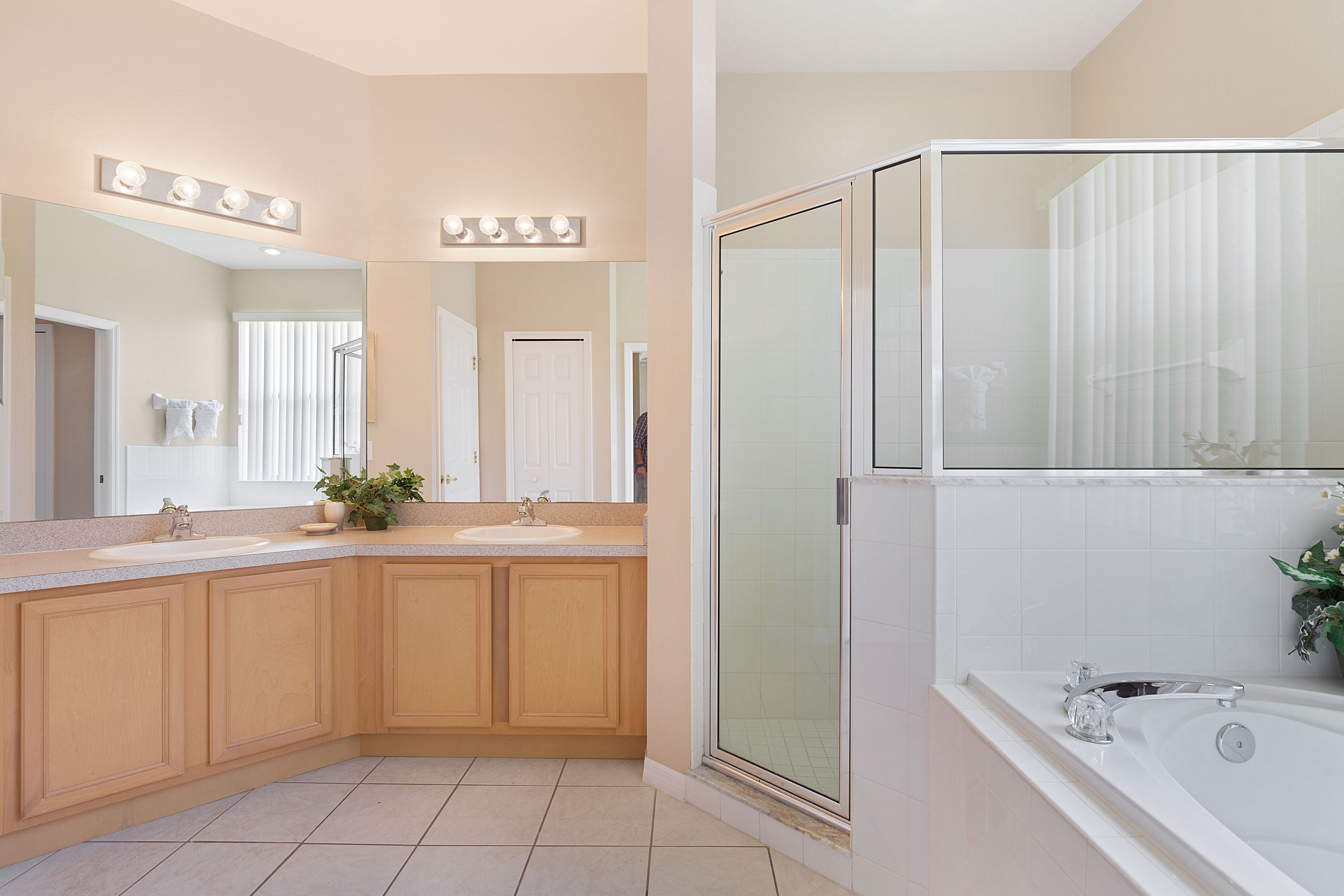 A modern bathroom with two sinks, a large mirror with lights, a glass-enclosed shower, and a bathtub.