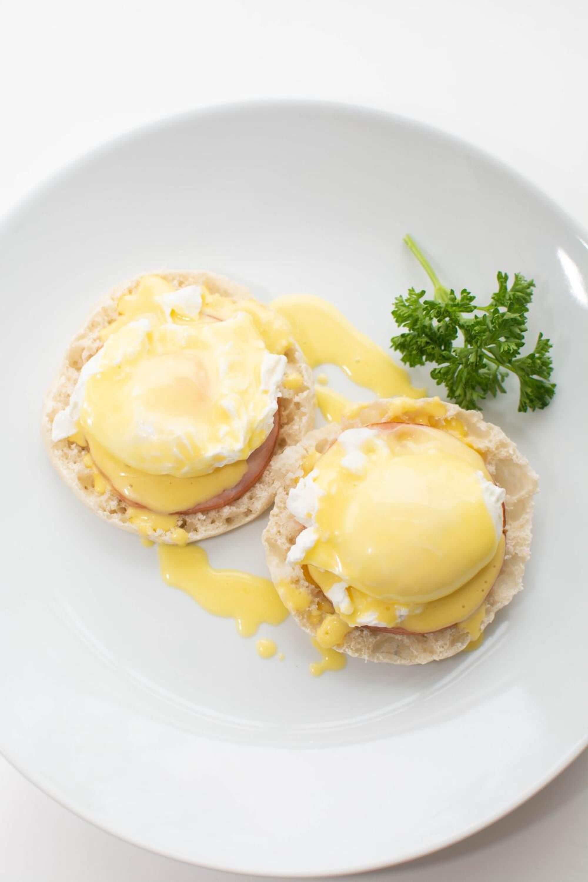 Een bord met twee Eggs Benedict sandwiches en een takje peterselie.