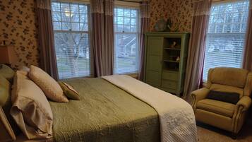 A bedroom with a bed, a green wardrobe, a yellow armchair, and floral wallpaper.