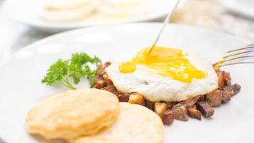Un plato con un desayuno que incluye huevos fritos, patatas ralladas y bizcochos.