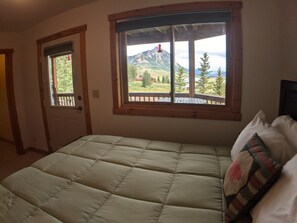 A bedroom with a bed, a window with a mountain view, and a door.