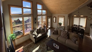 A spacious living room with large windows, a ceiling fan, and a cozy seating area. - Getaway in CB @ the Alpine Edge Retreat! 4 bedroom Single Family Home.  (Crested Butte)