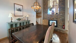 A dining area with a large wooden table, chairs, a chandelier, a fireplace, and a stone accent wall. - Getaway in CB @ the Alpine Edge Retreat! 4 bedroom Single Family Home.  (Crested Butte)