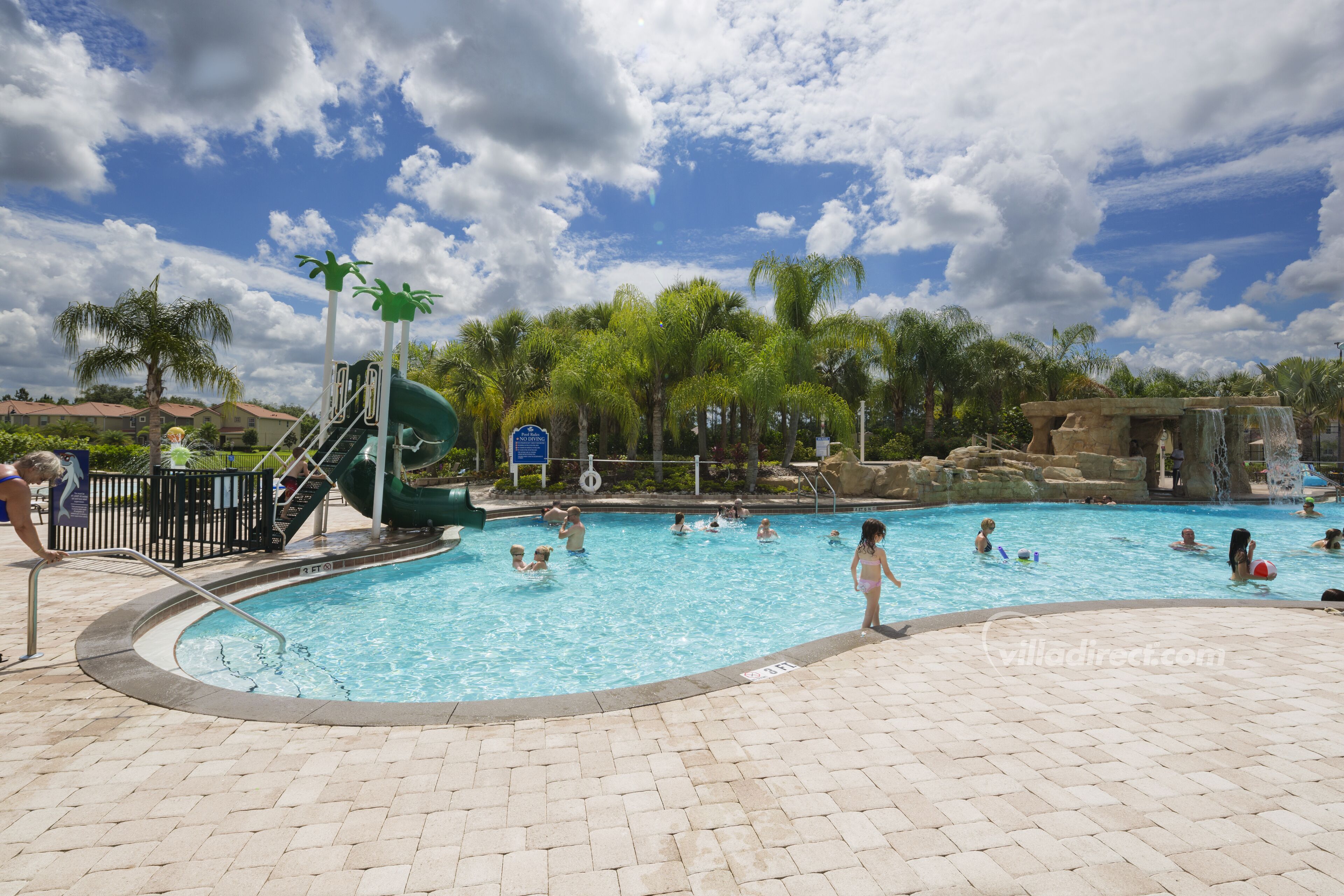 A swimming pool with a water slide, palm trees, and a clear sky.