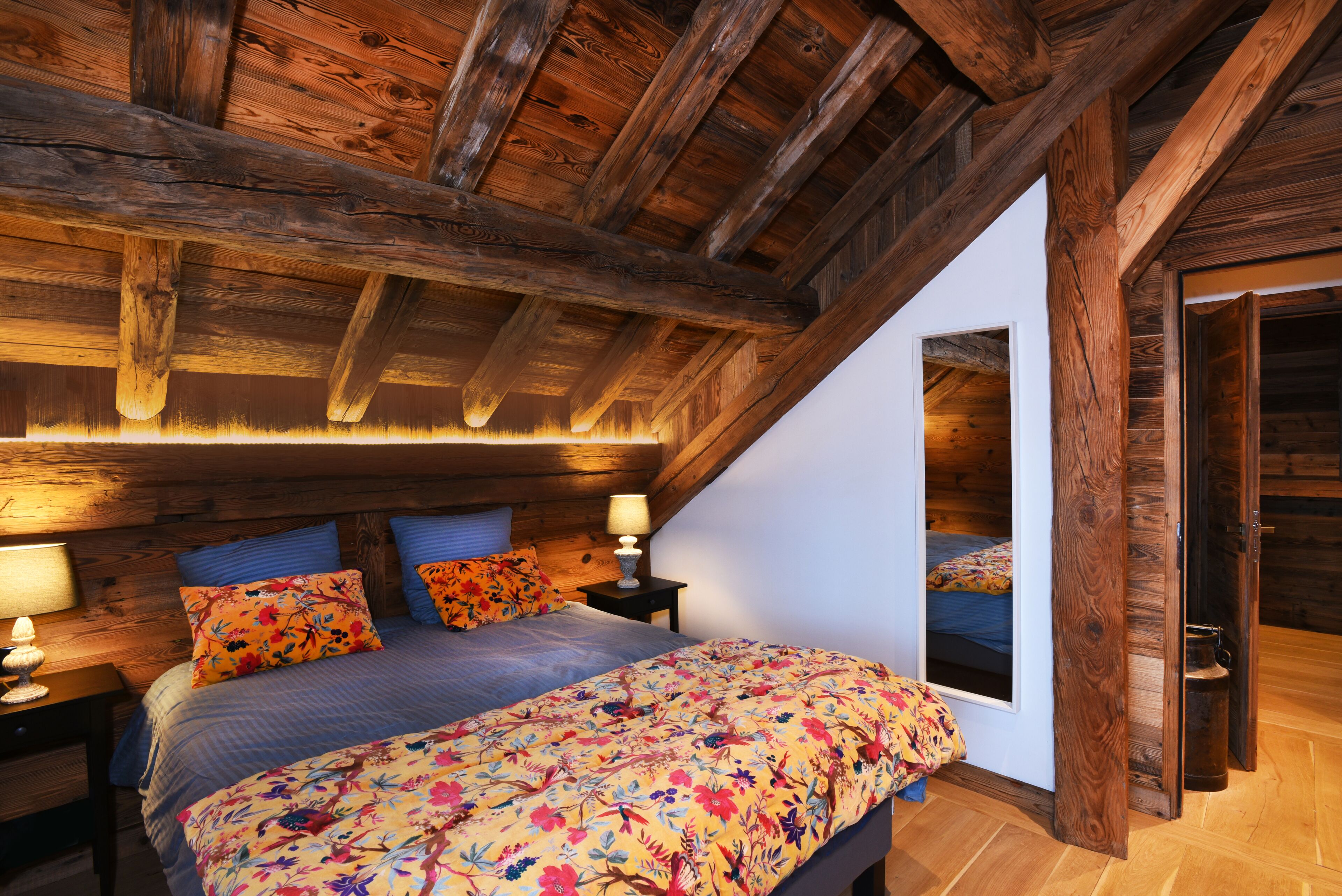 Un dormitorio con techo de madera, una cama con ropa de cama floral y dos mesitas de noche con lámparas.