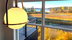 Ein Zimmer mit großem Fenster und Blick auf See und Wald.