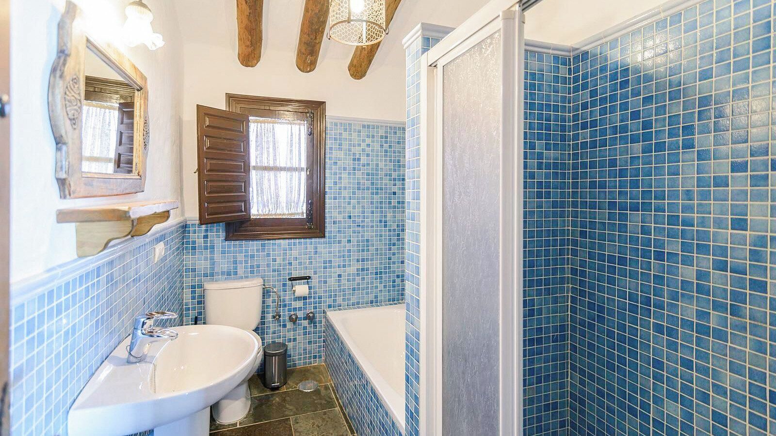 A bathroom with a sink, toilet, and bathtub, featuring blue mosaic tiles and wooden beams.