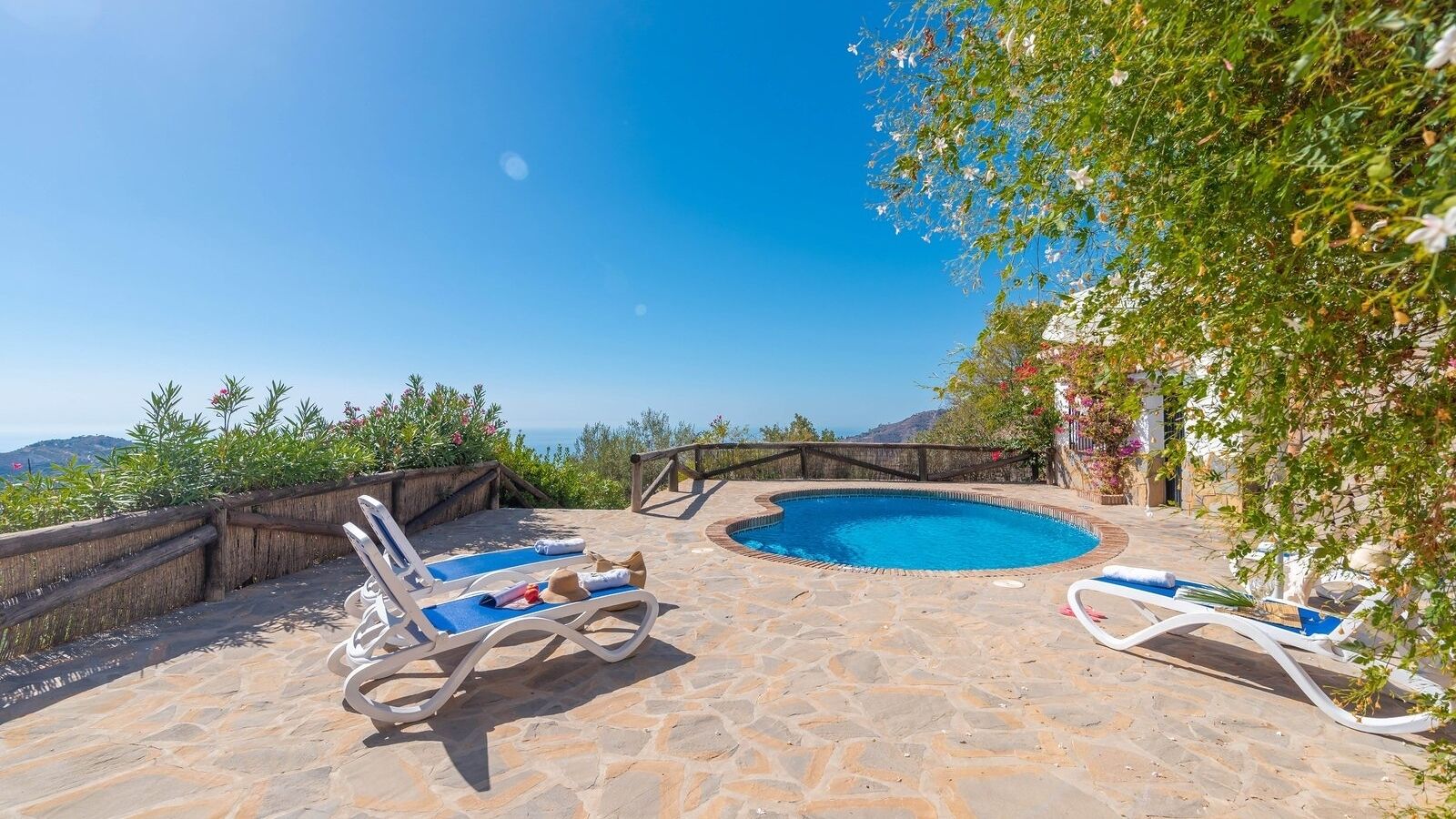 A stone pool with two lounge chairs, surrounded by a stone deck and a wooden fence.