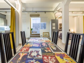 Un coin repas avec une table recouverte d’anciennes affiches, un escalier menant à un balcon et, au fond, une cuisine moderne.