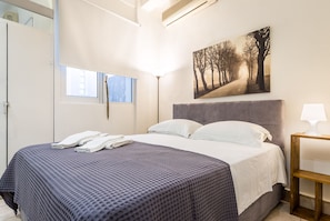 Une chambre à coucher avec un lit, une fenêtre, un tableau et une table de chevet avec une lampe.