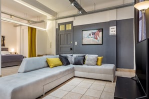 Un salon moderne avec un canapé d’angle gris, un téléviseur à écran plat et un tableau accroché au mur.