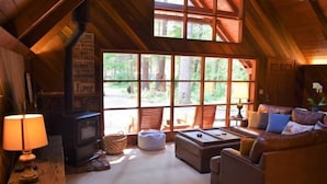 Interior acolhedor de cabana com lareira, assentos confortáveis e janelas amplas com vista para a floresta.