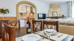 A dining area with a table set for two, a bottle of wine, and a television in the background. - Mirador de Cómpeta by Ruralidays (Málaga)