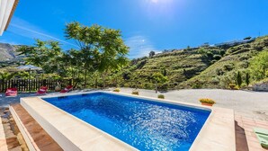A rectangular swimming pool with a clear blue water surface, surrounded by a wooden deck and red lounge chairs. - Mirador de Cómpeta by Ruralidays (Málaga)