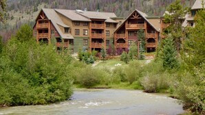 Un lodge con diverse strutture in legno, un fiume sullo sfondo e una montagna boscosa all'orizzonte.