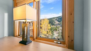 A room with a large window offering a view of a forested mountain range.