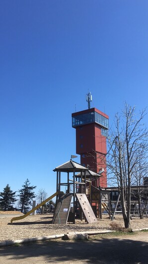 Une aire de jeux avec un toboggan et des structures d’escalade, une tour rouge dotée d’une partie en verre, et des arbres sans feuilles.