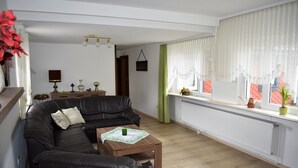 Una sala de estar con un sofá de cuero negro, una mesa de centro de madera y una ventana con cortinas translúcidas.