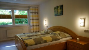Un dormitorio con una cama de madera, una mesita de noche, una lámpara de pared y una ventana con persianas.