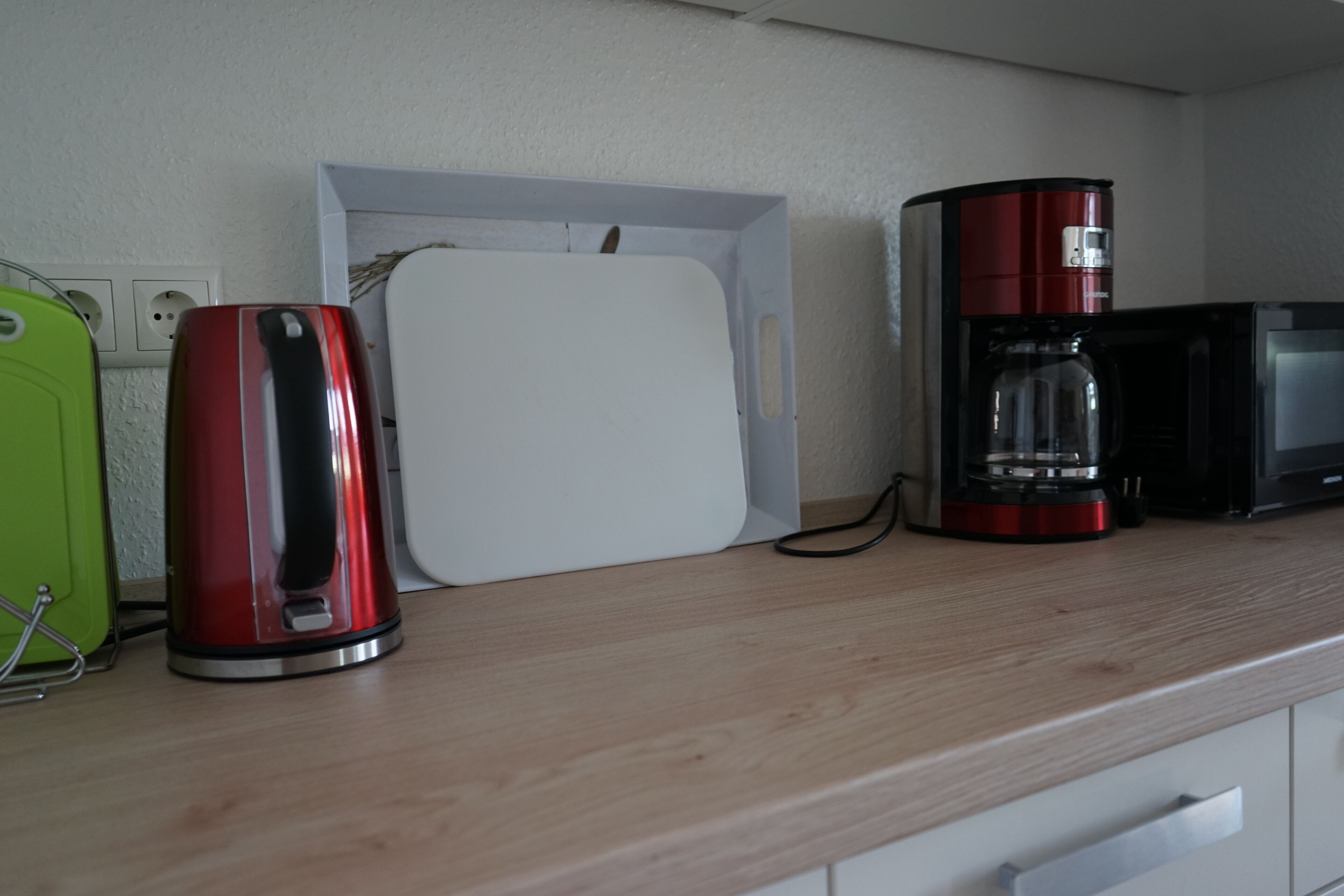 En köksbänk med en röd vattenkokare, en vit låda och en röd kaffebryggare.