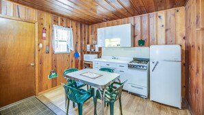 A compact kitchen with wooden walls, a dining table with chairs, and basic appliances including a refrigerator, stove, and microwave. - The Cabins at Cloudcroft (Cloudcroft)