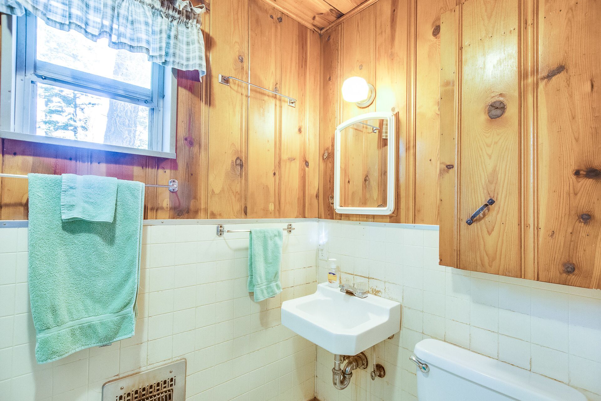 A wooden-paneled bathroom with a window, a sink, and a toilet.