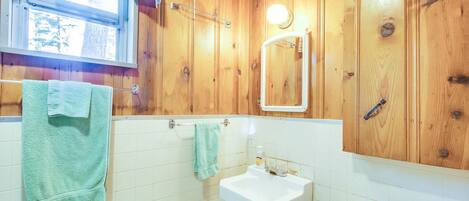 A wooden-paneled bathroom with a window, a sink, and a toilet.