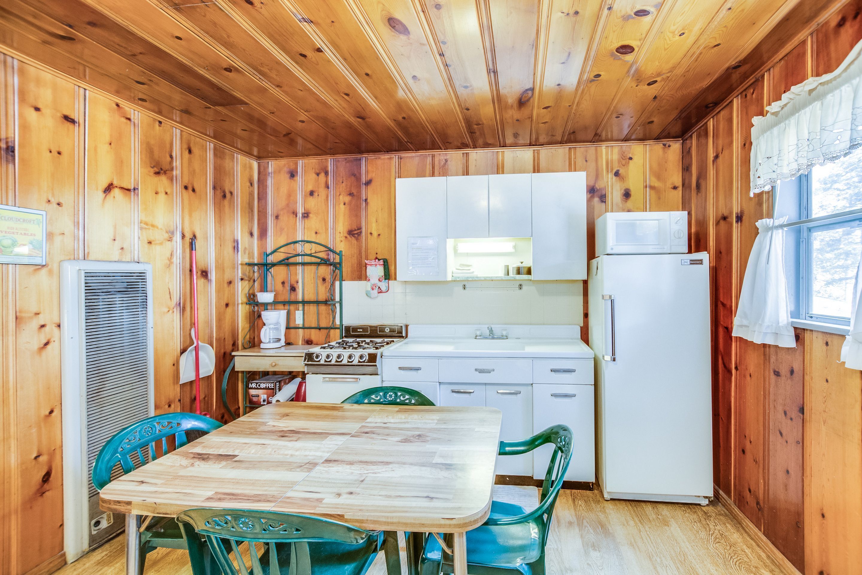 Une cuisine aux murs lambrés, avec une table et des chaises en bois, un fourneau, un four à micro-ondes et un réfrigérateur.