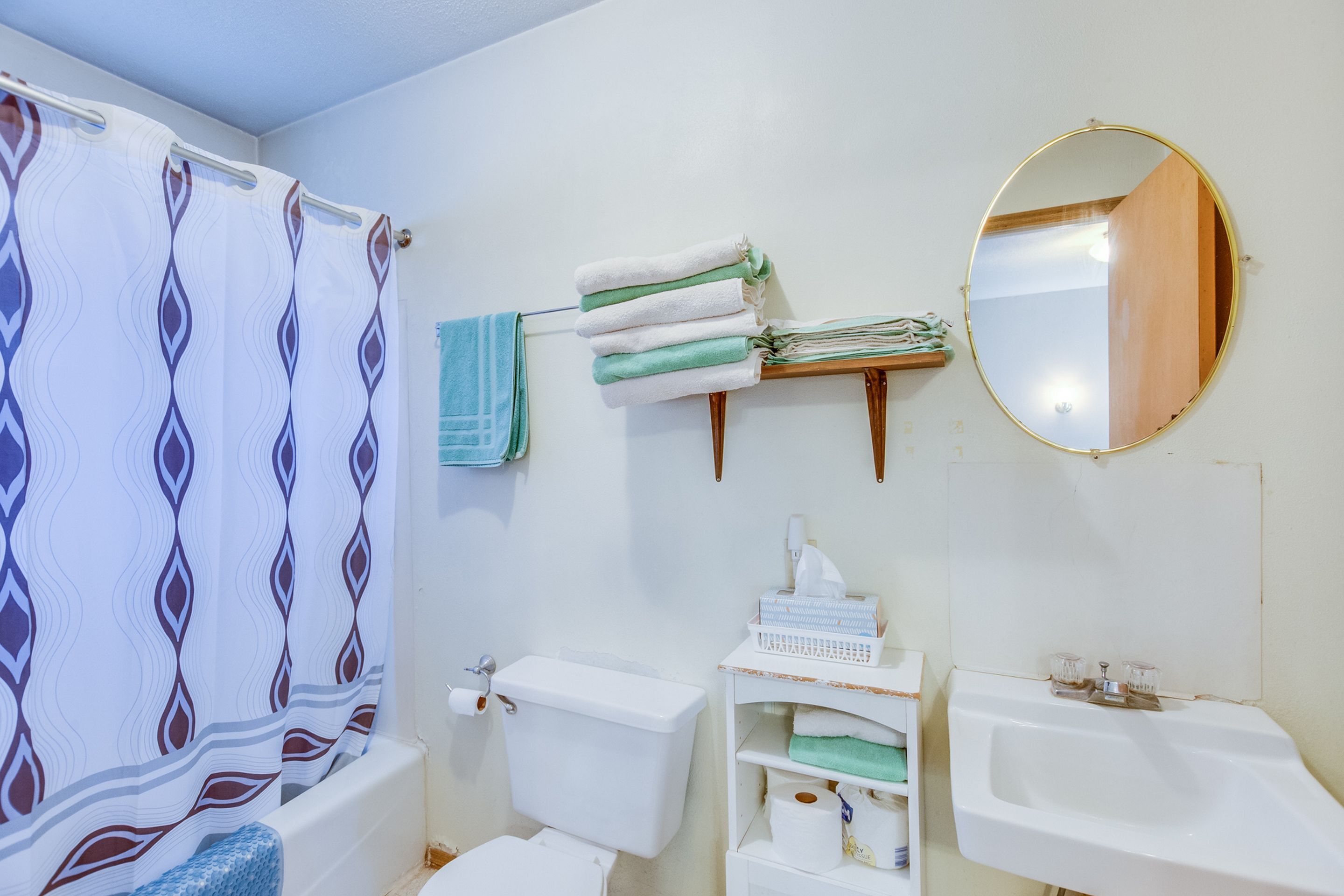 Une salle de bain avec un rideau de douche, des toilettes, un lavabo et un miroir.