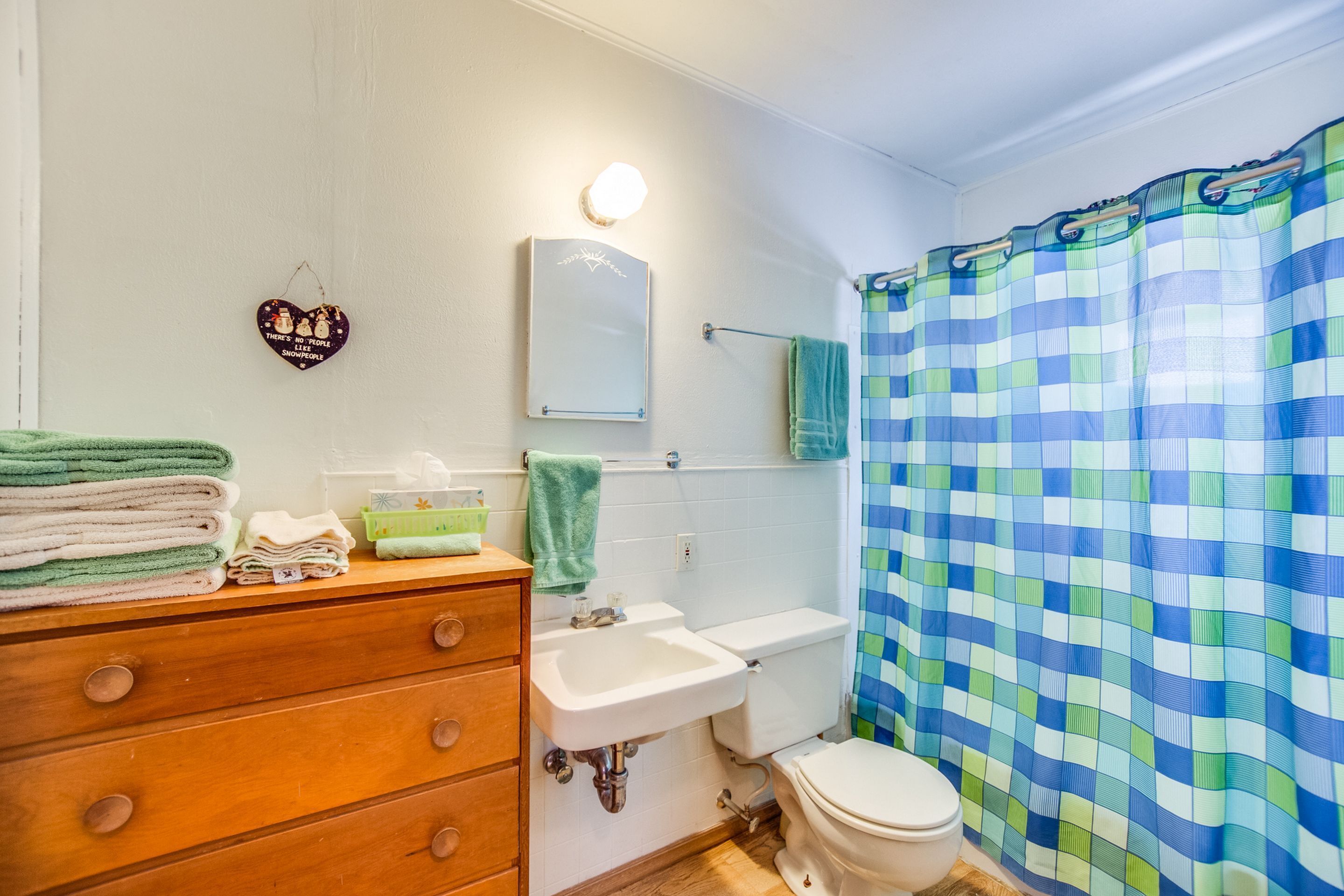 Un baño con tocador de madera, lavabo, inodoro y cortina de ducha a cuadros azules.