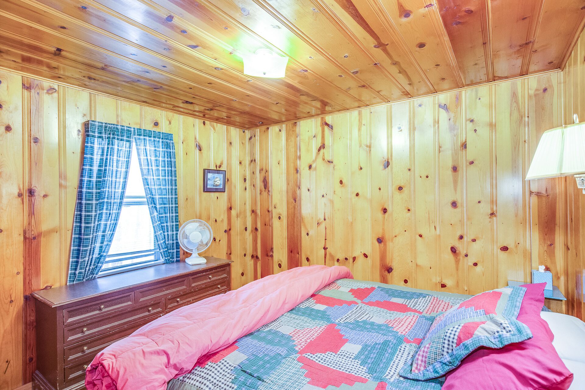 A wooden-paneled room with a bed, dresser, and window with curtains.