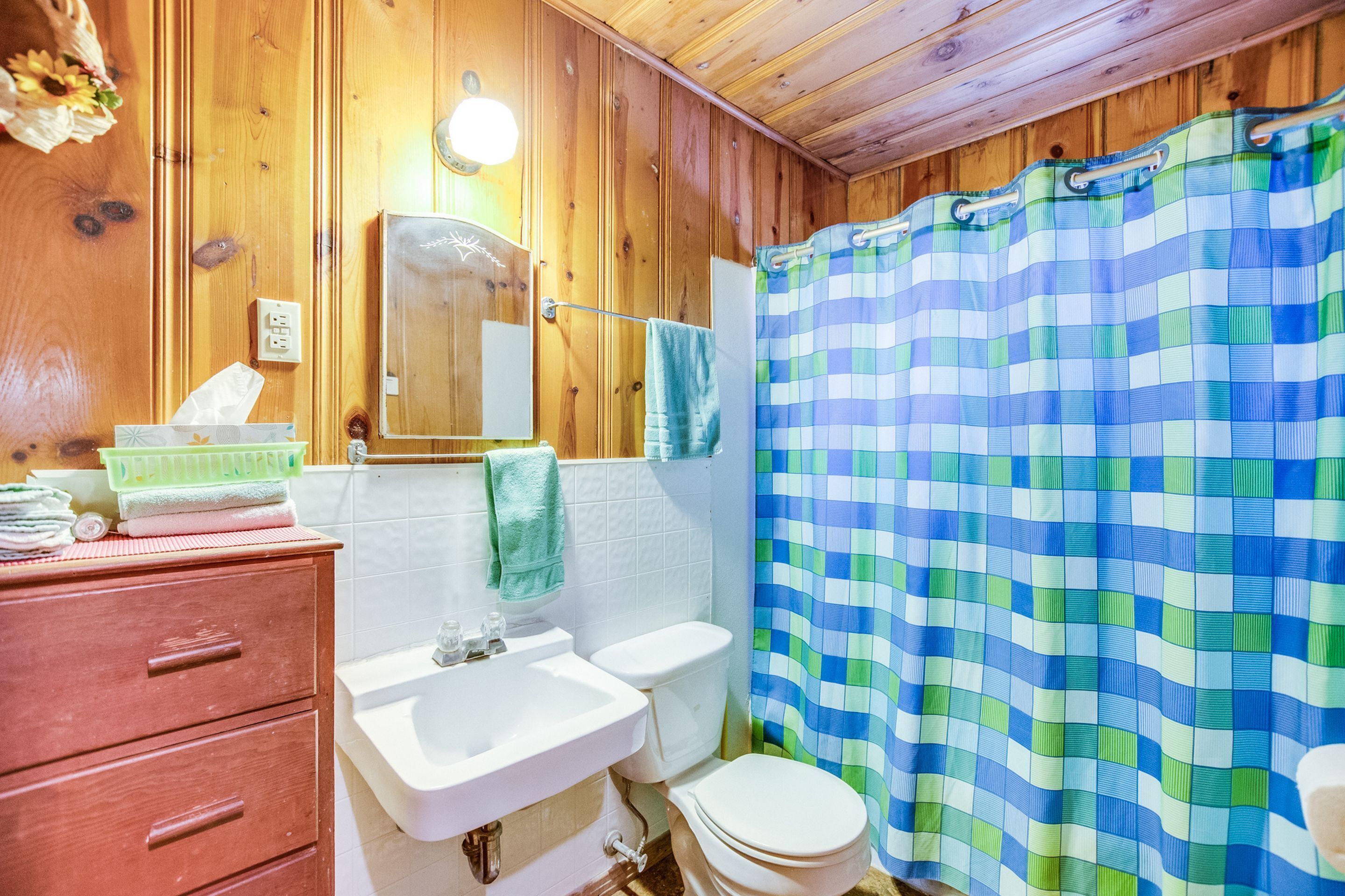 A wooden-paneled bathroom with a white sink, a mirror, and a toilet.