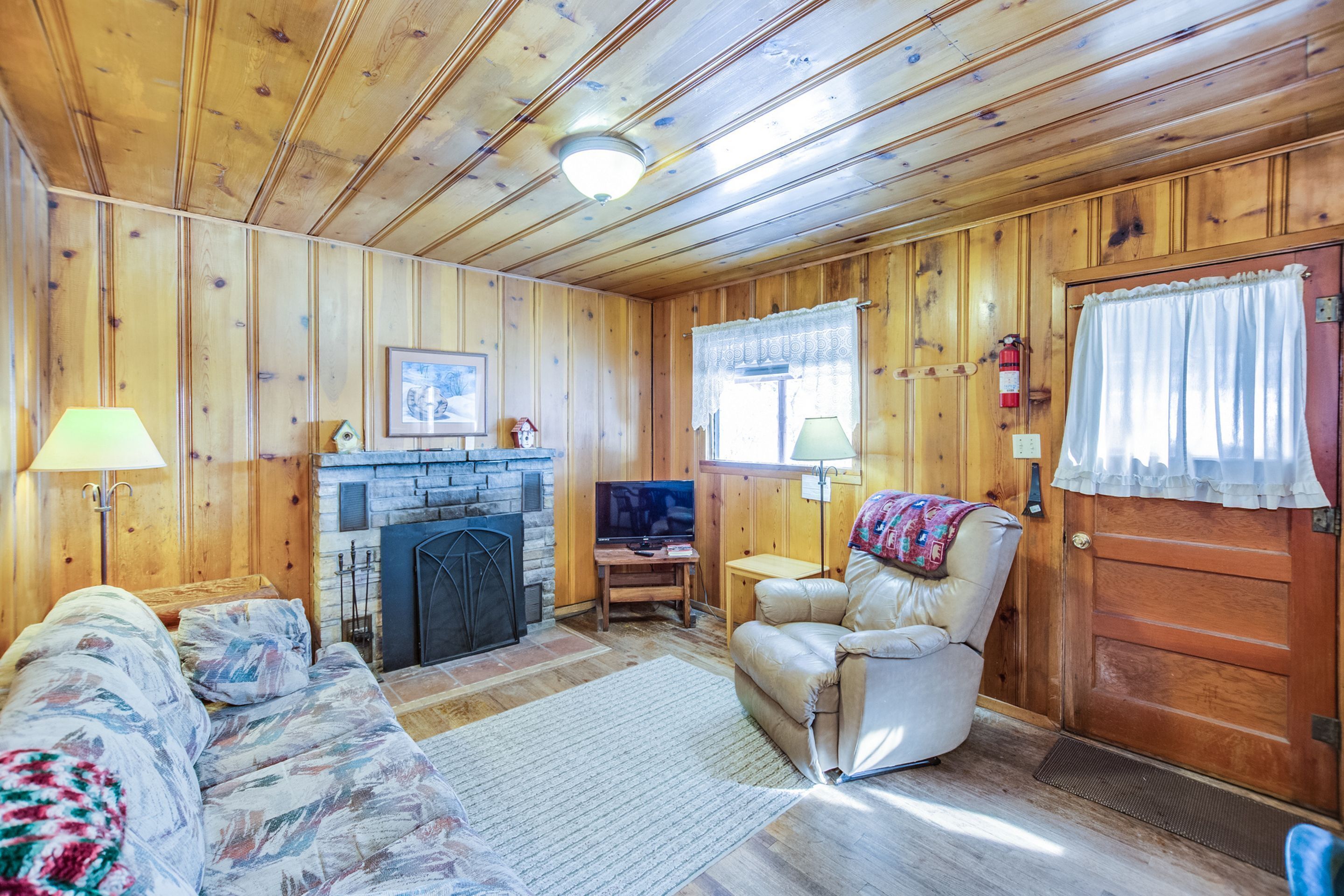 L’intérieur d’un chalet confortable, avec une cheminée, un téléviseur, un canapé et un fauteuil.