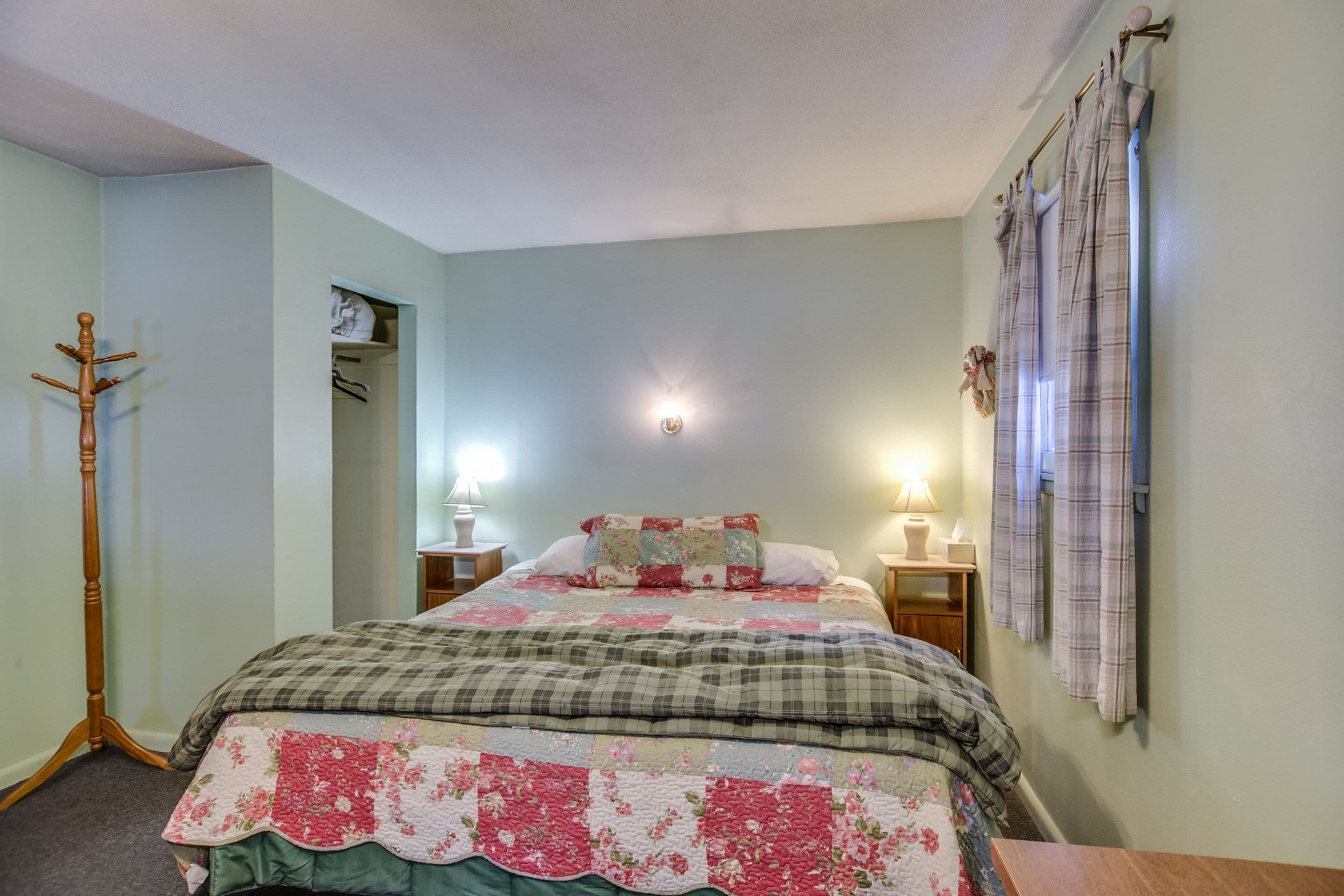 Een slaapkamer met een bed, twee nachtkastjes, een kapstok en een wandlamp.
