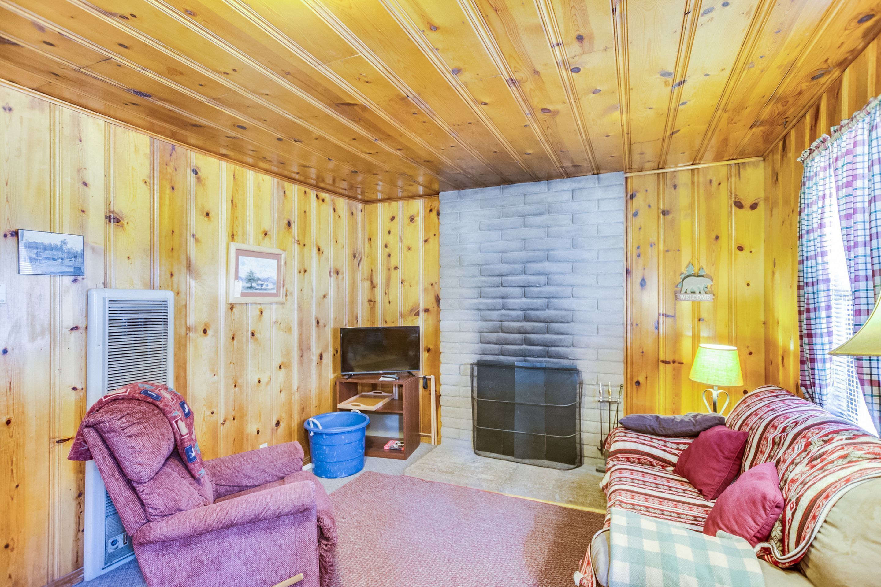 A cozy room with wooden walls, a fireplace, a sofa, a chair, and a television.