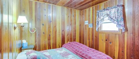 A wooden-paneled room with a bed, a nightstand, a lamp, and a window with a curtain.