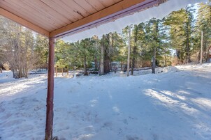 Un espacio al aire libre cubierto con techo de madera, rodeado de nieve en el suelo y altos árboles.