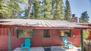 A rustic cabin with a metal roof, two windows, and a door. There are two turquoise chairs outside. - The Cabins at Cloudcroft (Cloudcroft)