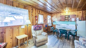 A cozy cabin interior with a wooden interior, a dining area, a kitchen with a refrigerator, and a window with a lace curtain. - The Cabins at Cloudcroft (Cloudcroft)