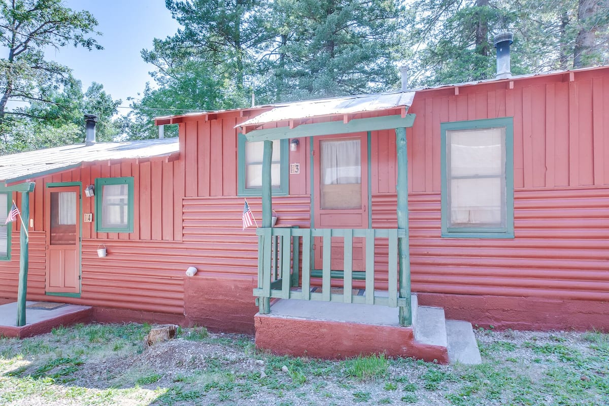 Eine rote Holzhütte mit Veranda, einer Haustür und einem Fenster.