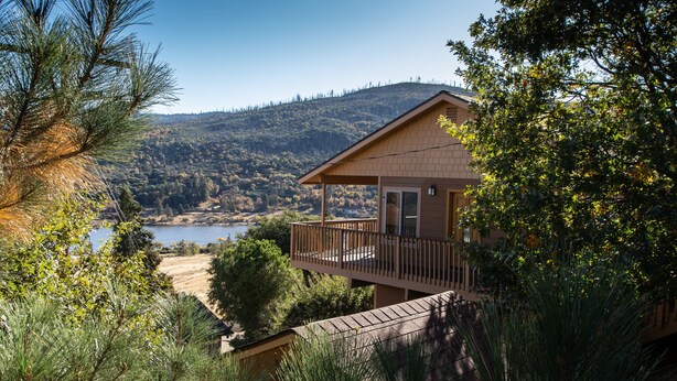 Una casa de dos pisos con un balcón que da a un lago y colinas.