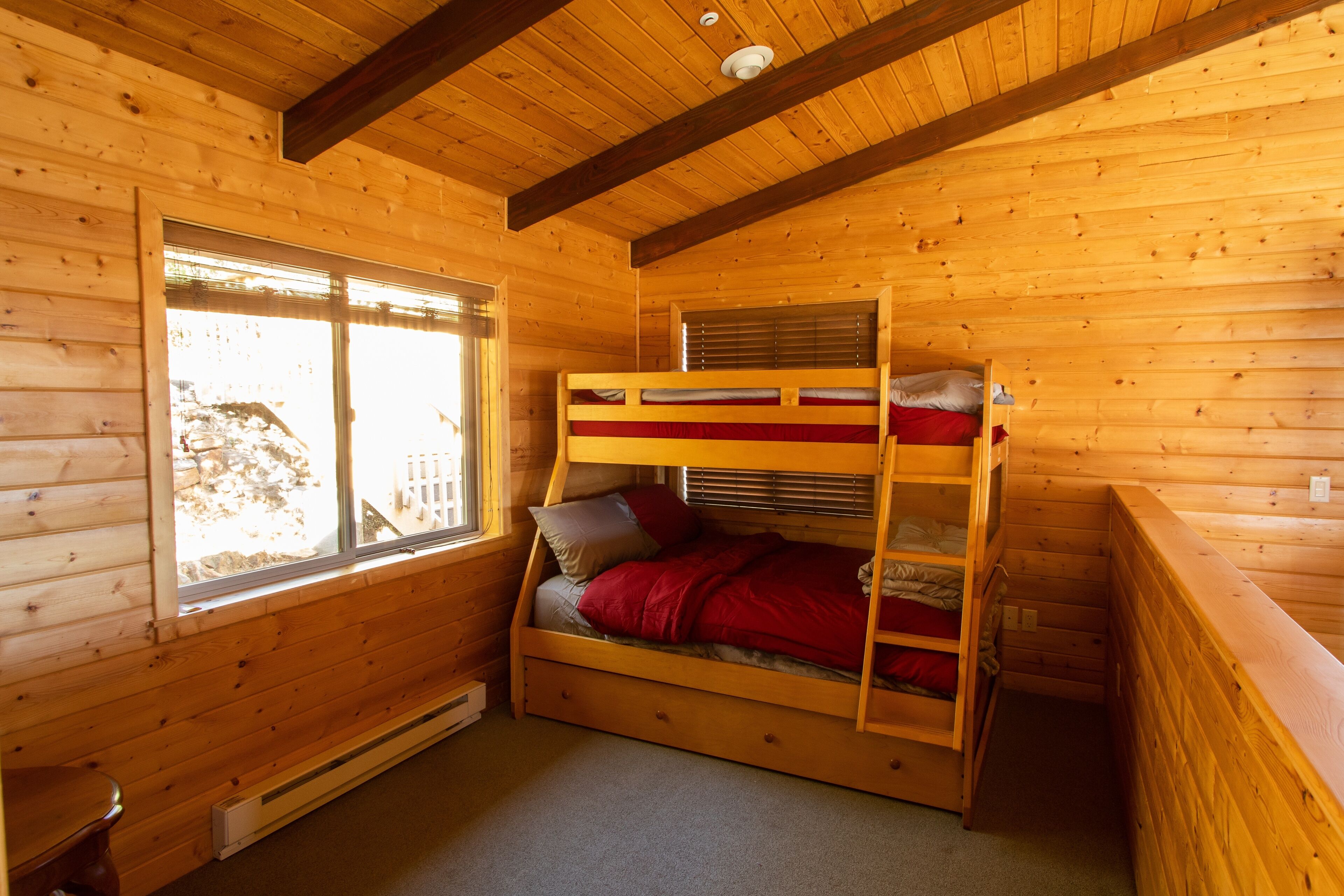 Une chambre dans un chalet en bois, avec un lit superposé, une fenêtre et un radiateur.