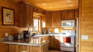 Cocina de cabaña de madera con una isla central, microondas empotrado, estufa y un amplio ventanal que proporciona luz natural.