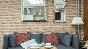 A cozy room with a brick wall, a sofa with cushions, a small table with a cup and saucer, and a lamp. - Fantastic apartment in Barrio de las Letras (Madrid)