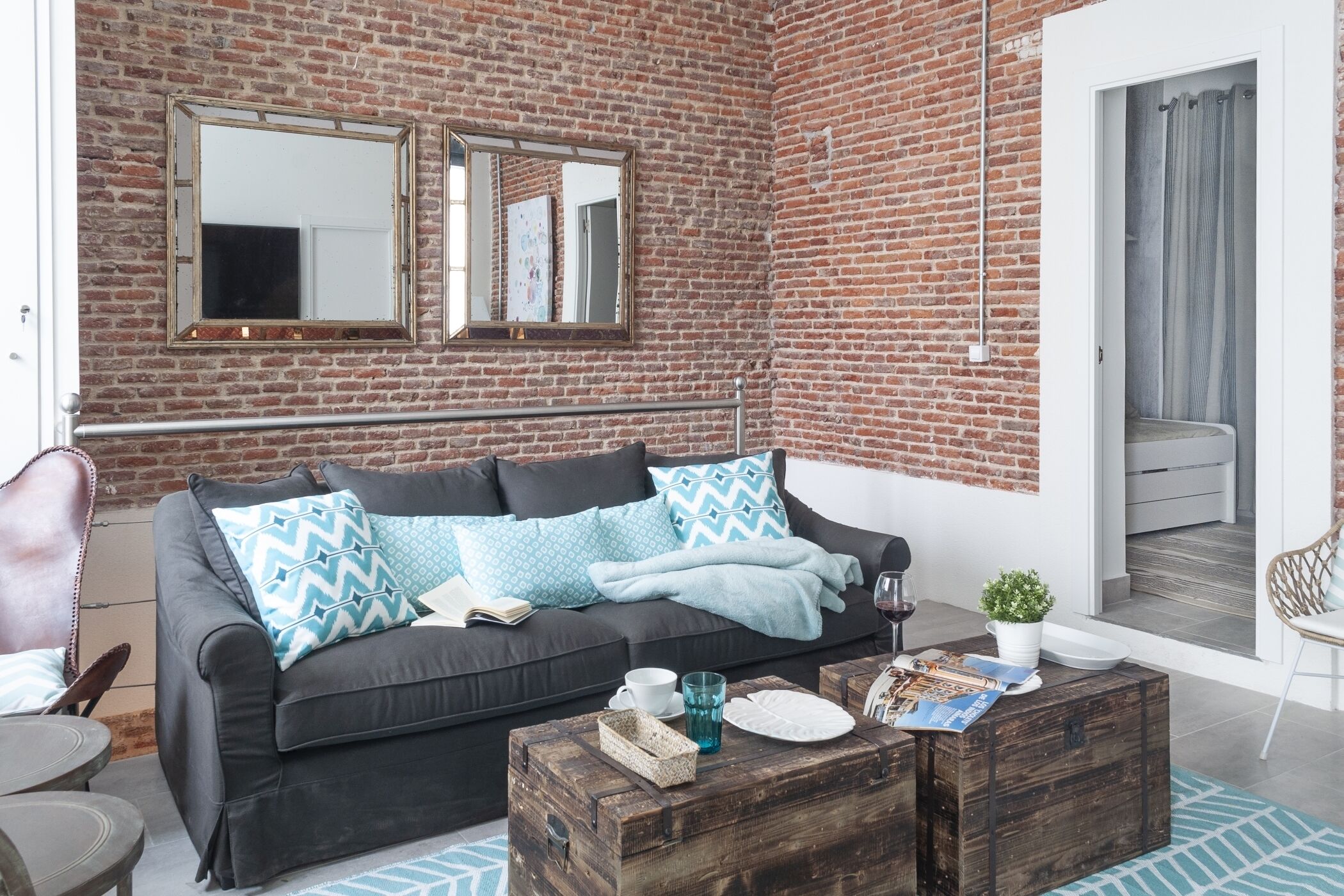 A cozy living area with a brick wall, a dark sofa with patterned cushions, a wooden coffee table, and a white chair.