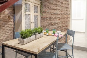 Mesa de madeira com cadeiras, plantas em vasos e parede de tijolos.