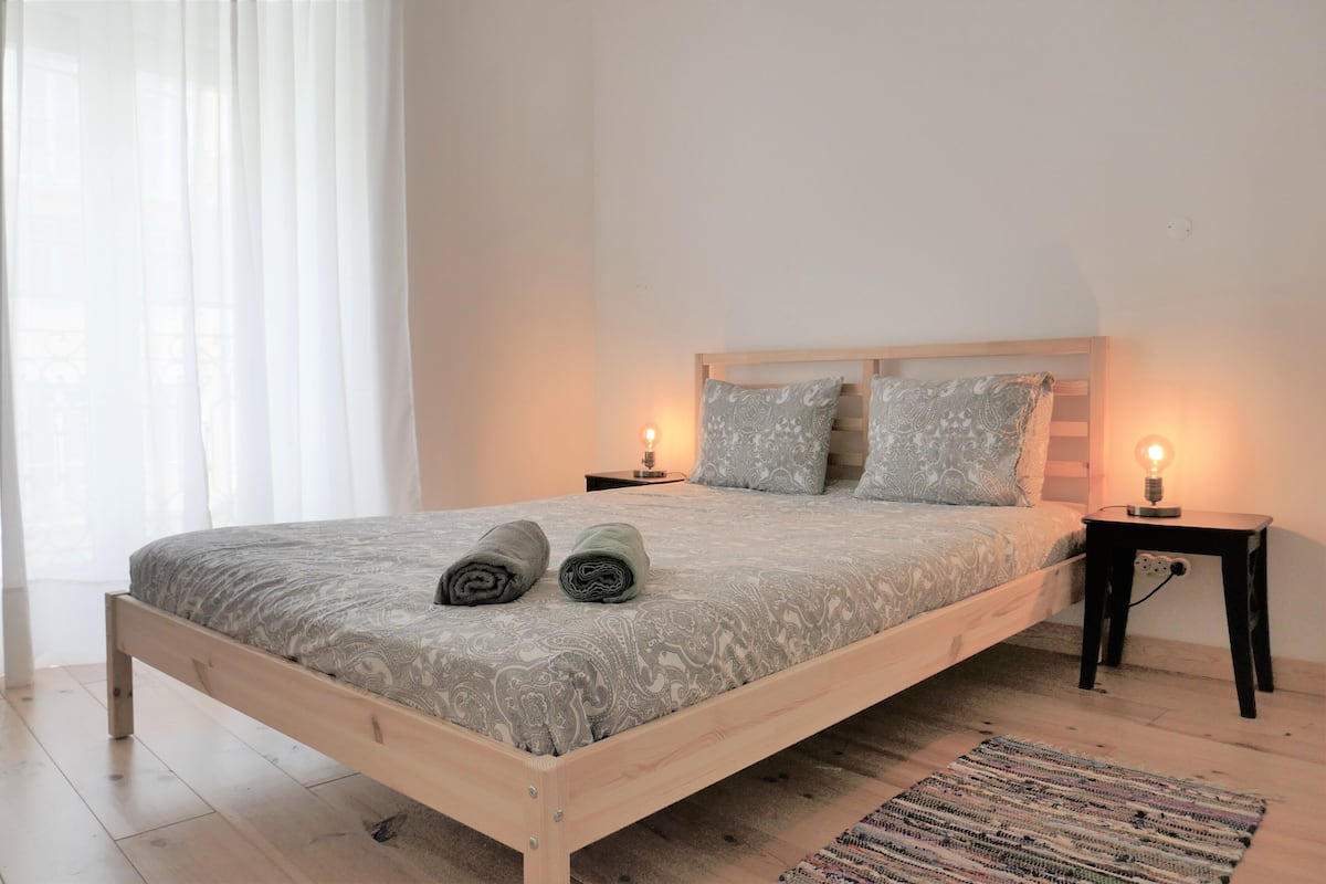 Une chambre à coucher avec un lit en bois, deux tables de chevet avec des lampes, une couvre-lit à motifs et un tapis sur le sol.