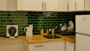 Une cuisine avec des meubles blancs, un plan de travail recouvert de carreaux verts, une machine à café et un évier.