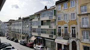 Une rangée d’immeubles à plusieurs étages dotés de balcons, une rue bordée de voitures garées et un ciel dégagé.